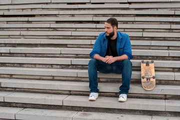 Young skater with beard chilling on the concrete steps