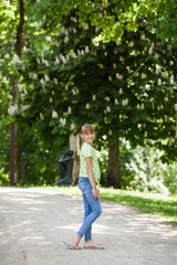 Fototapeta na wymiar Portrait of little smiling girl child walking outdoor in park at sunny day in spring. Blooming chestnut tree in the background. Teen is wearing jeans and green shirt. Lifestyle shot in nature. 