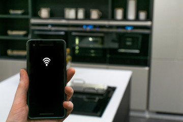 Hand using smart phone as smart home control application over blurred kitchen background, smart home concept