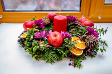 Unique handmade magic Christmas wreath with a red candle on the background of a winter window