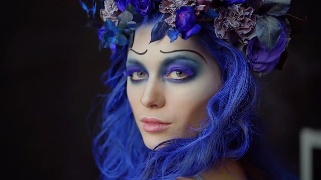 Portrait of beautiful woman wearing fantastic makeup for halloween, beautiful flowers in a blue hair.