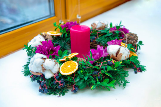 Unique handmade magic Christmas wreath with a pink candle on the background of a winter window