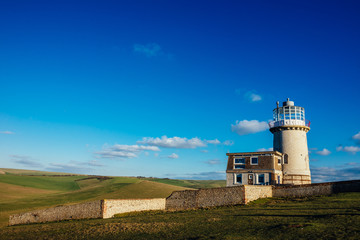 Fototapeta na wymiar The Belle Tout Lighthouse located at Beachy Head, East Sussex, United Kingdom with a clean blue sky and clouds on the scene - Seven Sisters National Park