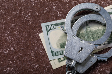Dollars and handcuffs on a stone surface with copy space, top view