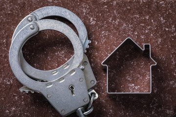 Handcuffs and a figure in the shape of a house on a stone surface. Concept on real estate fraud