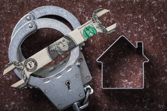 Handcuffs with a dollar and a figure in the shape of a house on a stone surface. Concept on the topic of real estate fraud