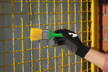 Worker painting metal protective net to yellow color, closeup of hand with paintbrush 