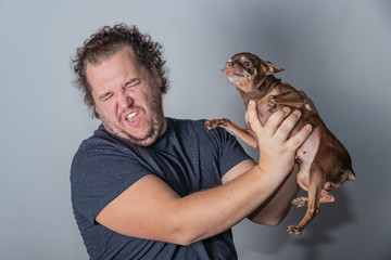 Obraz premium Funny fat man poses with little dog on gray background