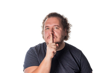 Portrait of handsome man cowering his mouth with his finger and looking at camera while standing against white background