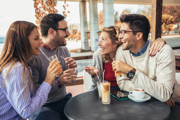 Group of four friends having fun a coffee together. Two women and two men at cafe talking laughing and enjoying their time