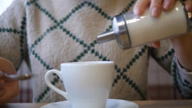 A woman stirs sugar in tea with a spoon in a white mug