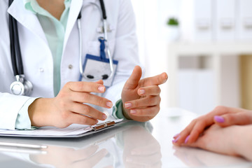 Doctor and patient talking while sitting at the desk in hospital office, close-up of human hands. Medicine and health care concept