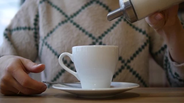 Woman puts sugar in tea in a white mug