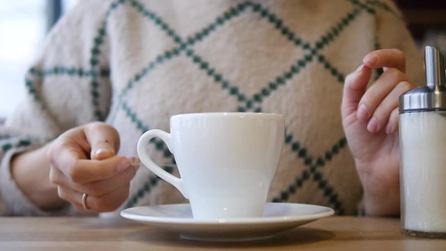 A woman stirs sugar in tea with a spoon in a white mug