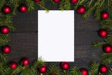 Fototapeta na wymiar Dark rustic wooden table background with white card and Christmas decoration - fir and red ornament frame. Top view with free space for copy text