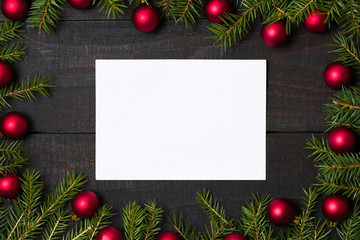 Fototapeta na wymiar Dark rustic wooden table background with white card and Christmas decoration - fir and red ornament frame. Top view with free space for copy text