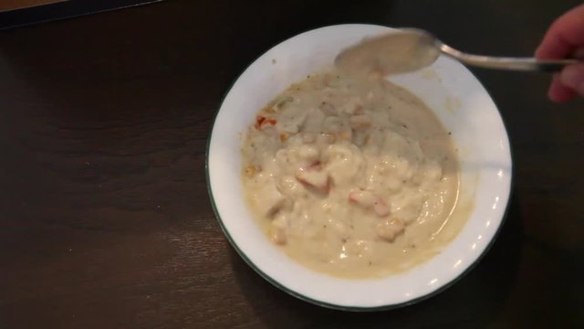 A white bowl is full of delicious looking corn chowder and is stirred 