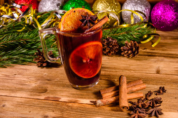 Cup of mulled wine with cinnamon, christmas decorations and fir tree branches on wooden table