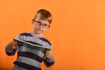 Portrait of a boy in glasses with a book in his hands, a cheerful schoolboy on a yellow background.