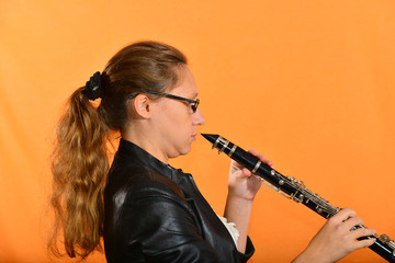 Girl in glasses in a black jacket plays the clarinet.