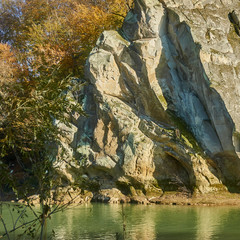 A fragment of a rock (called a cockerel) is reflected in the clear water of a mountain river on a sunny day. Close-up of a fragment of rock. Autumn landscape with mountain river and rock