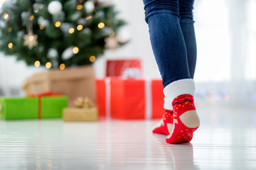 Woman in woolen socks going to christmas gift boxes under xmas tree