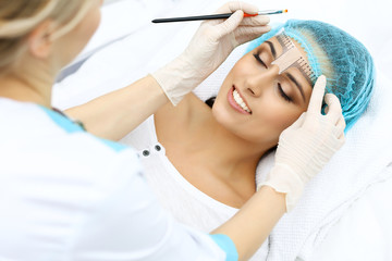 Naklejka premium Professional beautician is going to correct eyebrow line at woman face using cosmetic ruler. Permanent brow makeup in beauty salon, closeup. Cosmetology treatment