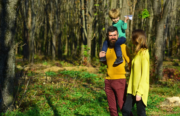 Adventure is out there. Mother and father piggybacking little son enjoy sunny day in park during...