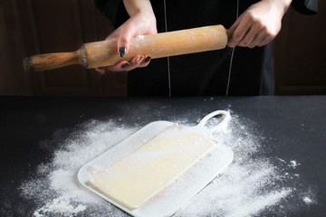 Man sprinkling flour over splinter on kitchen black table. The cook preparing buns at table in...