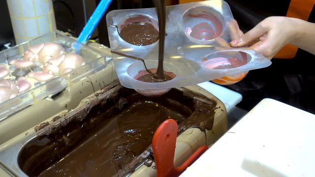 Professional confectioners womans pours warm melted chocolate in plastic molds. HD video