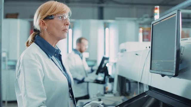 On High Tech Factory Female Engineer Uses Computer for Programing Pick and Place Electronic Machinery for Printed Circuit Board Surface Mount Assembly Line. Production of PCB with SMT Machinery.