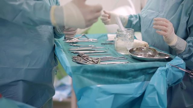 Surgeon picks surgical instruments on a tray in a clinic.