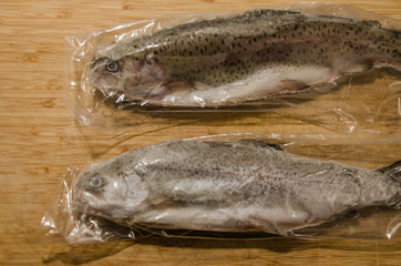 Sealed and frozen rainbow trout fish in plastic packing on wooden table in kitchen, ready for...