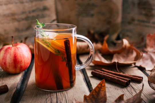 Apple tea, cinnamon sticks, wooden background, retro rustic style, autumn mood, fallen dry leaves