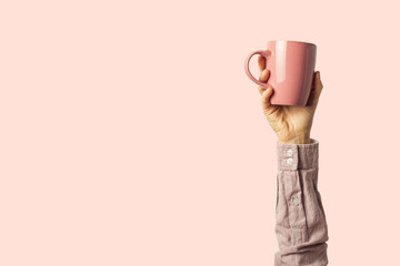 Female hand holding a purple cup with hot coffee or tea on a light pink background. Breakfast concept with hot coffee or tea