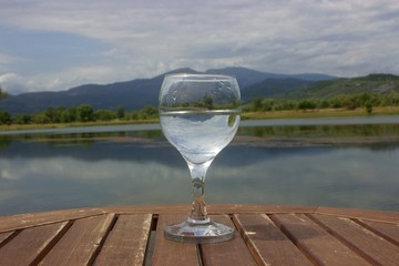 Glass of water on a wooden table with a background view of lake and a mountain
