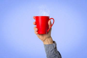 Male hand holding a red cup with hot coffee or tea on a light blue background. Breakfast concept with hot coffee or tea