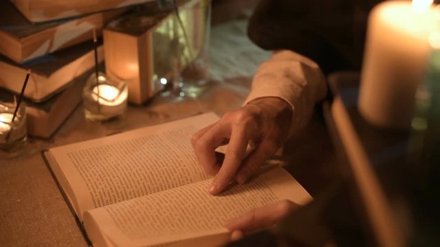 Big Close-up girl magician in a dark room with candlelight looking for a spell in a book. Low key live camera. Mystic. Small DOF