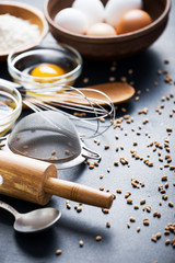 Baking ingredients. Bowl, eggs, flour, eggbeater, rolling pin and eggshells on black chalkboard from above.