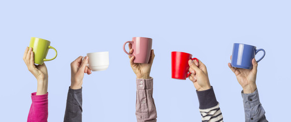 Many different hands holding multi colored cups of coffee on a blue background. Female and male hands. Concept of a friendly team, a coffee break, meeting friends, morning in the team. Banner