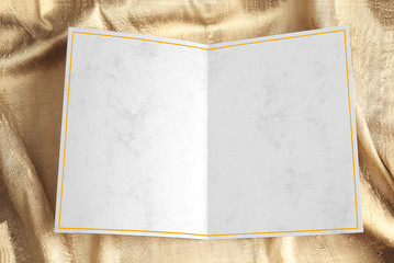 Blank open greeting card with yellow frame over gold draped fabric