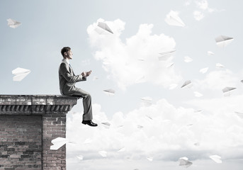 Man on roof edge send message with smartphone and cityscape at b