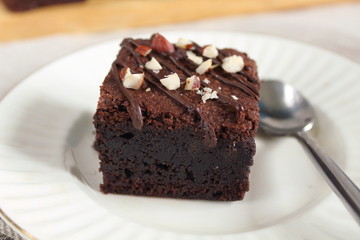 Chocolate fudgy brownie with nuts on white plate with spoon