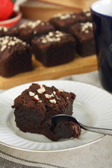Chocolate fudgy brownie with nuts on white plate with spoon