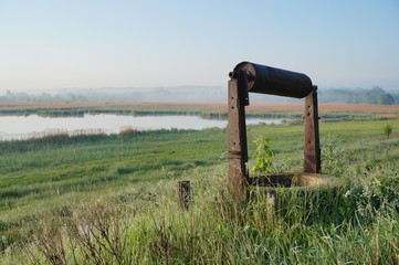 An old well in the foreground of a fall foliage landscape with trees on the horizon and mountains...