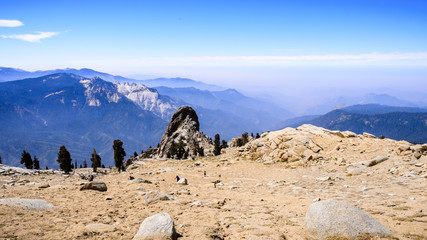 Aerial views of the hiking trail and the valley beyond as seen from Alta Peak in Sequoia National Park, Sierra Nevada mountains, California; smoke from wildfires visible in the background