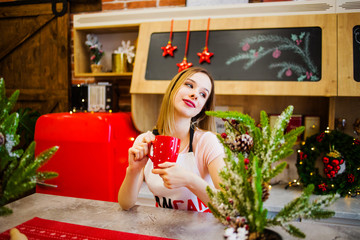 A charming blonde in a red apron holds a cup in her hands
