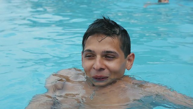  Cheerful view of a smiling young brunet man with short hair enjoying life in a wading pond with see-through celeste waters in summer in slow motion