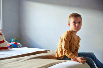 Portrait of boy sitting on bed against wall at home © Cavan for Adobe