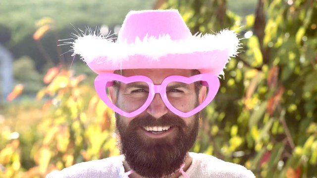 Comic man with funny hipster pink sunglasses and comic pink hat. Bearded crazy man looking at the camera. Make funny face. Cowboy.